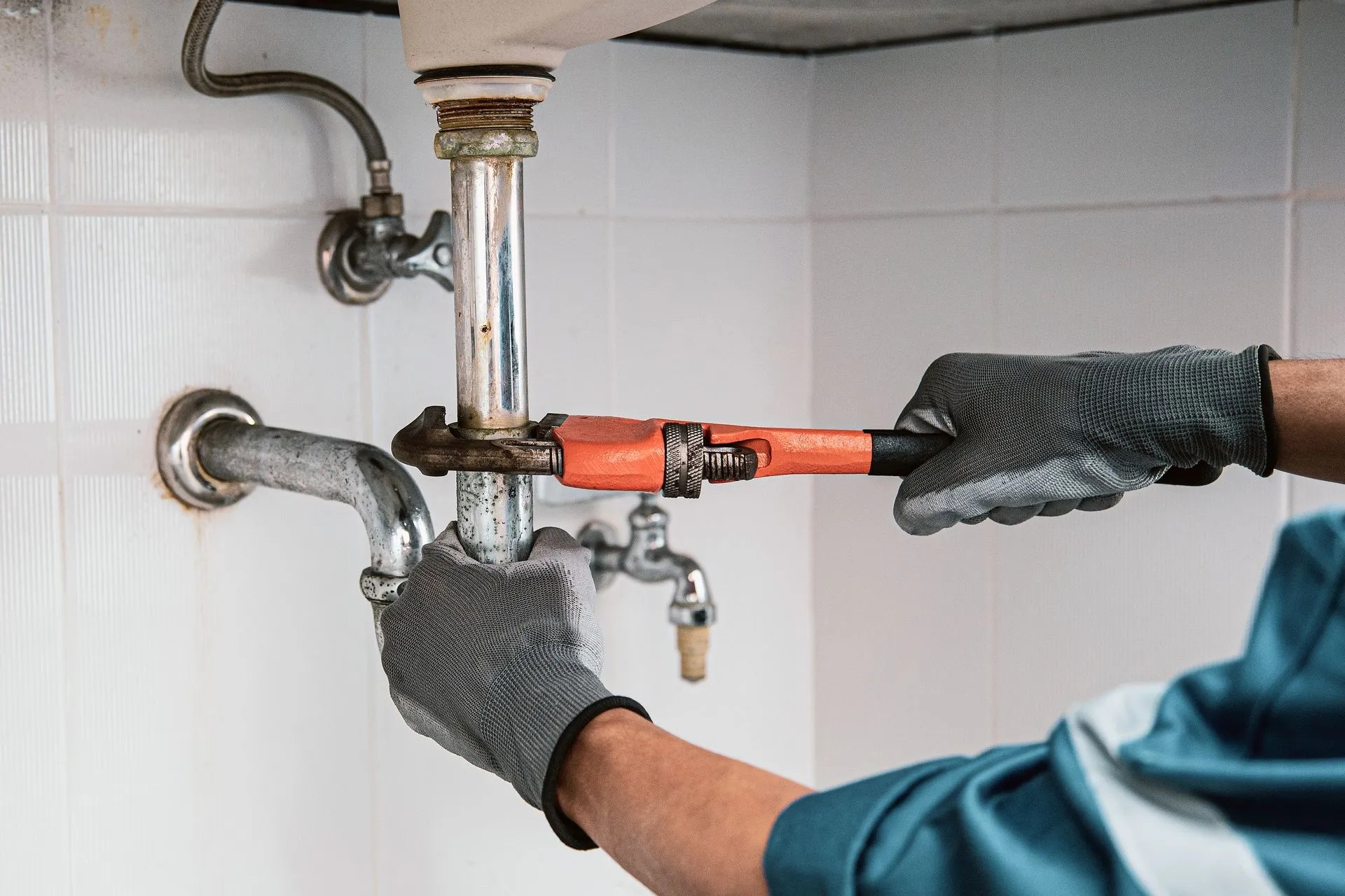 Plumber tightening a chrome drain pipe with a pipe wrench