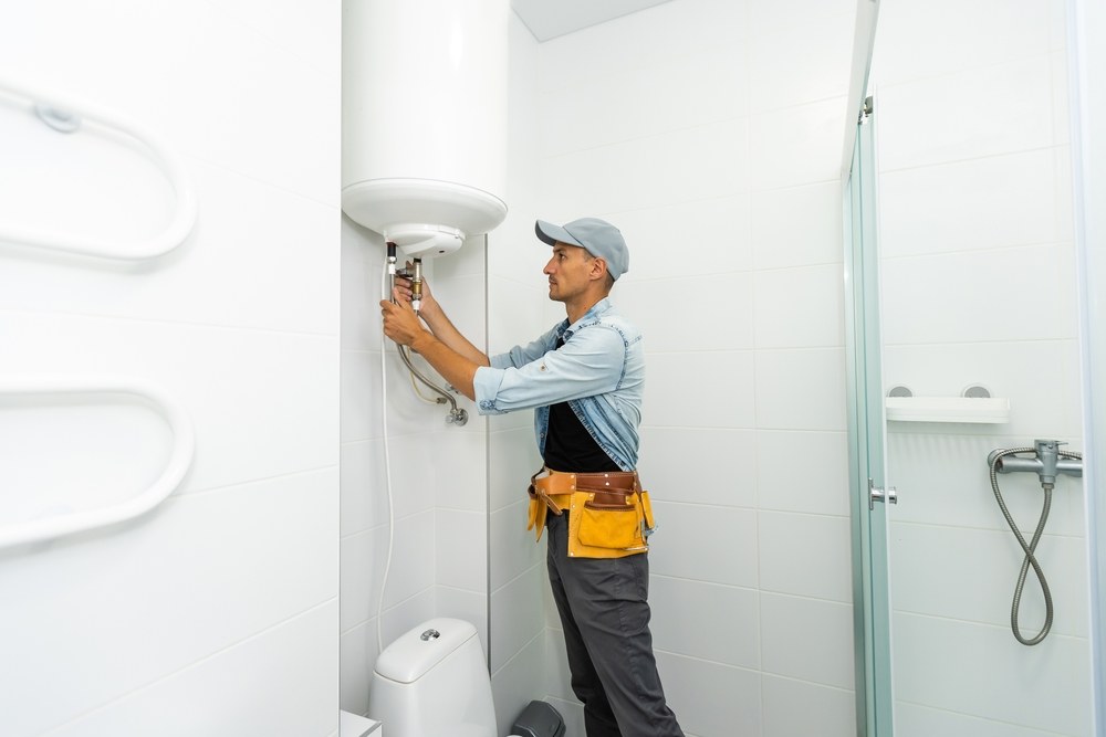 Technician servicing a white water heater in a bright tiled bathroom
